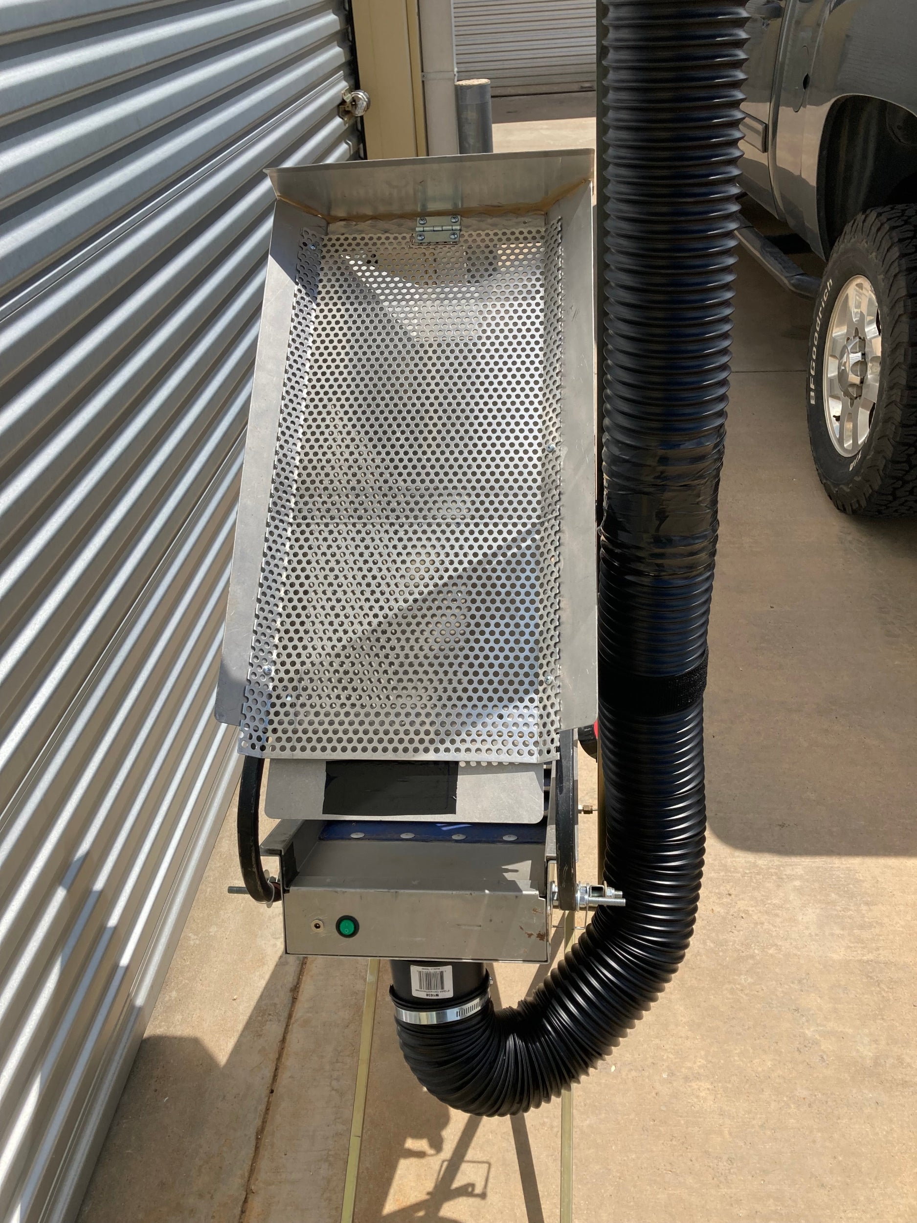 Close-up of the Snorkel 12V Drywasher showing the perforated hopper, green power switch, and 4″ snorkel hose connected to the internal blower on a tripod stand.