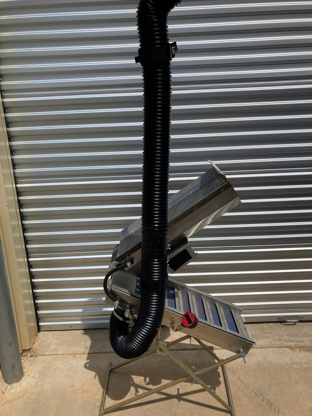 Full view of the Snorkel 12V Drywasher with the 4″ snorkel hose raised vertically ~6 ft, aluminum body, and tripod stand beside a corrugated wall.