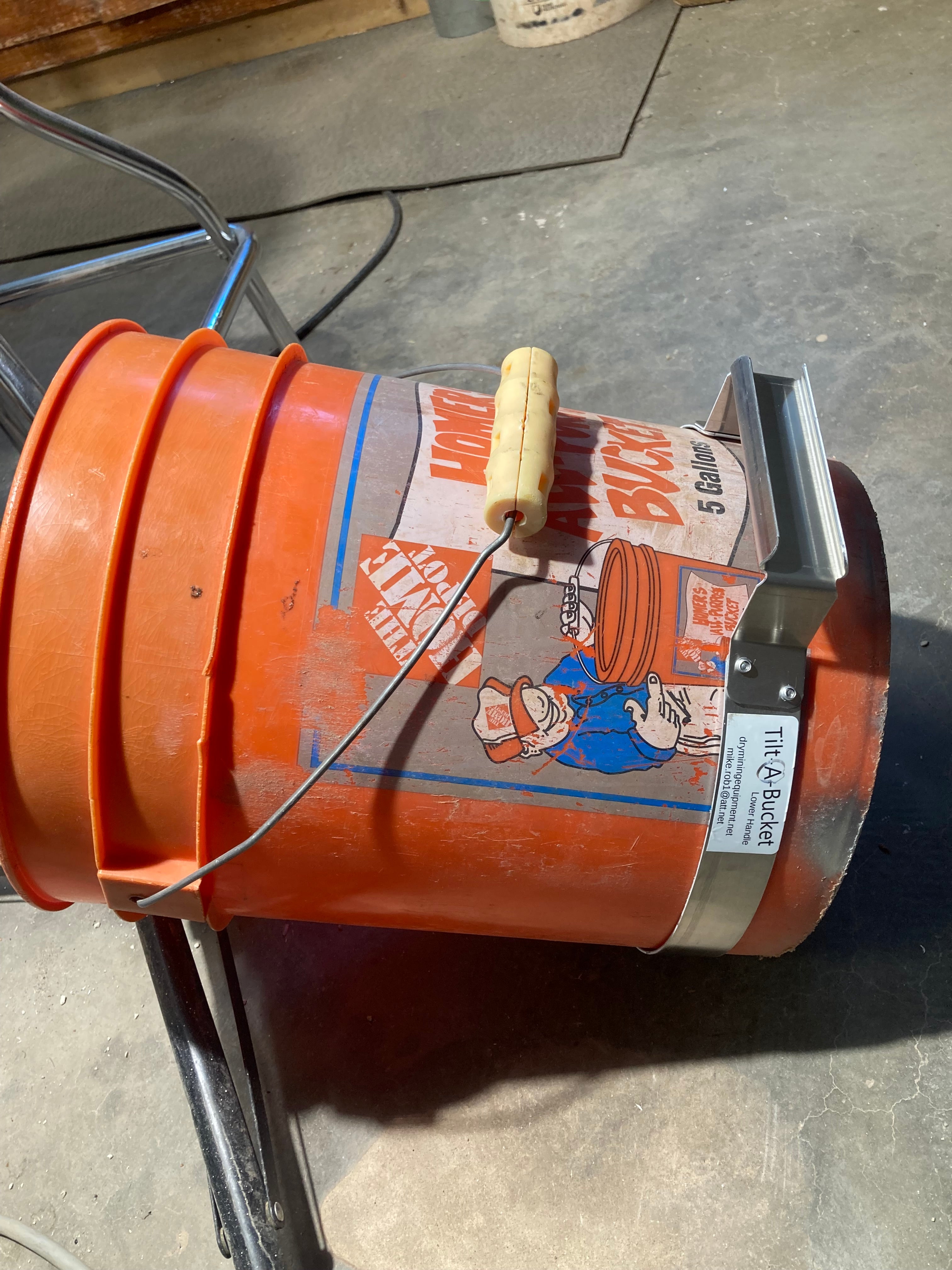 Aluminum Tilt-A-Bucket lower handle ring fitted on a 5-gallon plastic bucket for dual-point lifting and controlled pouring.